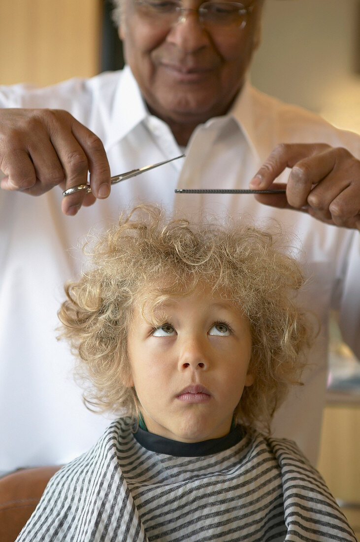 Friseur schneidet einem Jungen vorsichtig die Haare
