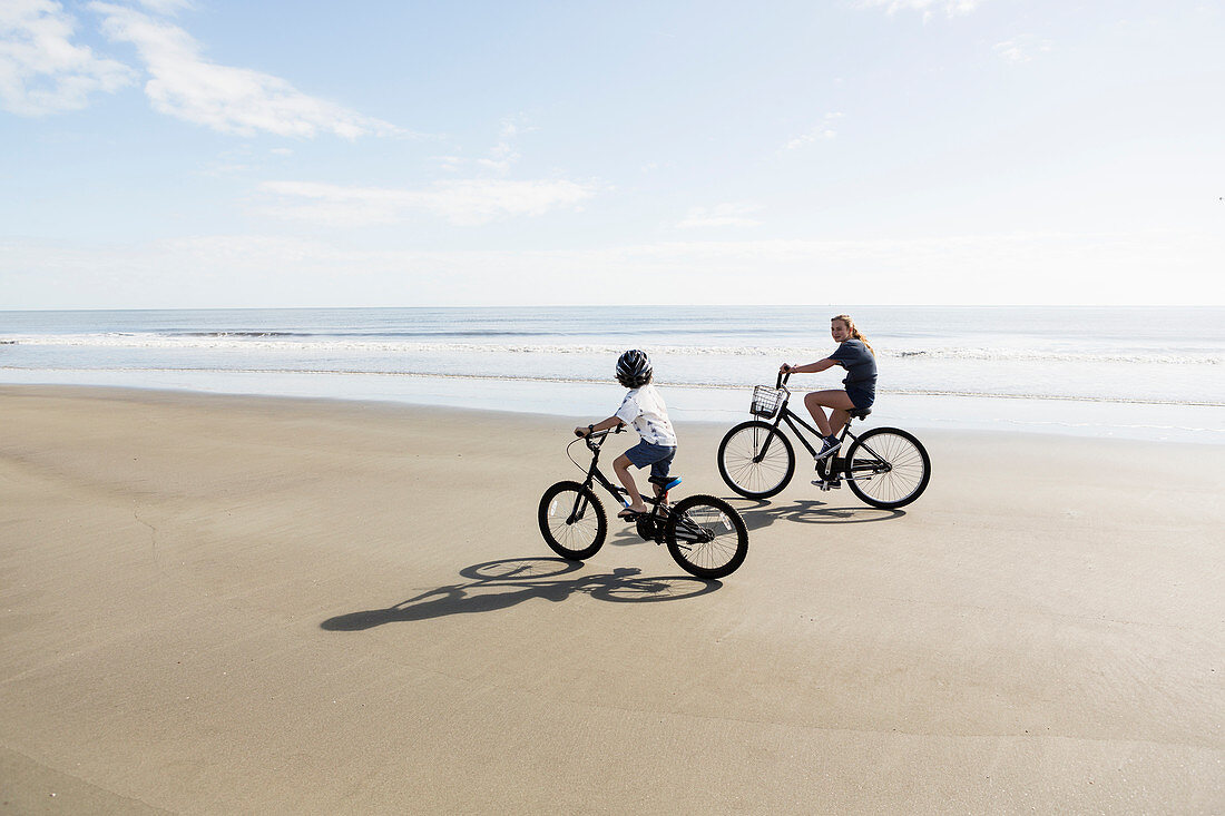 Geschwister, ein Junge und ein Mädchen, fahren mit Fahrrädern am Strand entlang