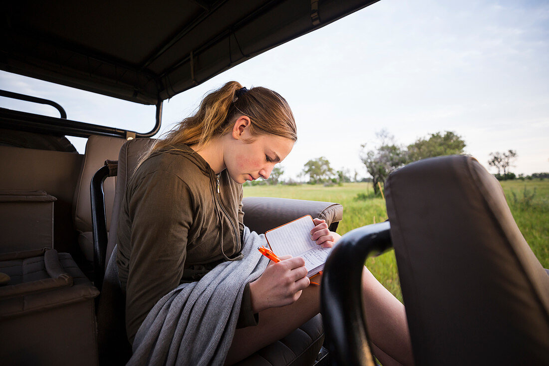 Ein junges Mädchen schreibt im Safari-Jeep im Busch in ihr Tagebuch