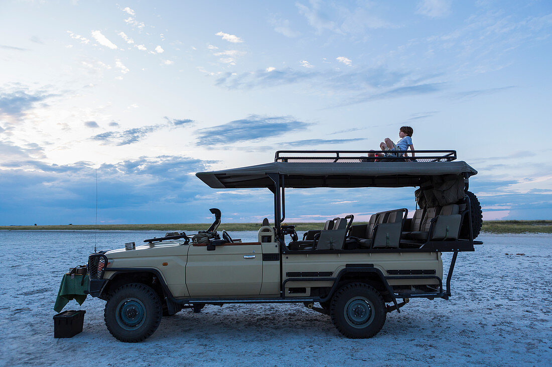 Ein sechsjähriger Junge und seine Schwester im Teenageralter sitzen in der Abenddämmerung auf einem Safari-Jeep