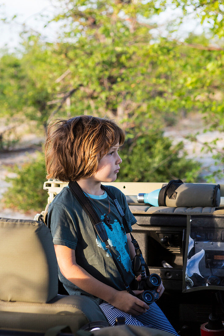 A five year old boy holding binoculars in a safari jeep.