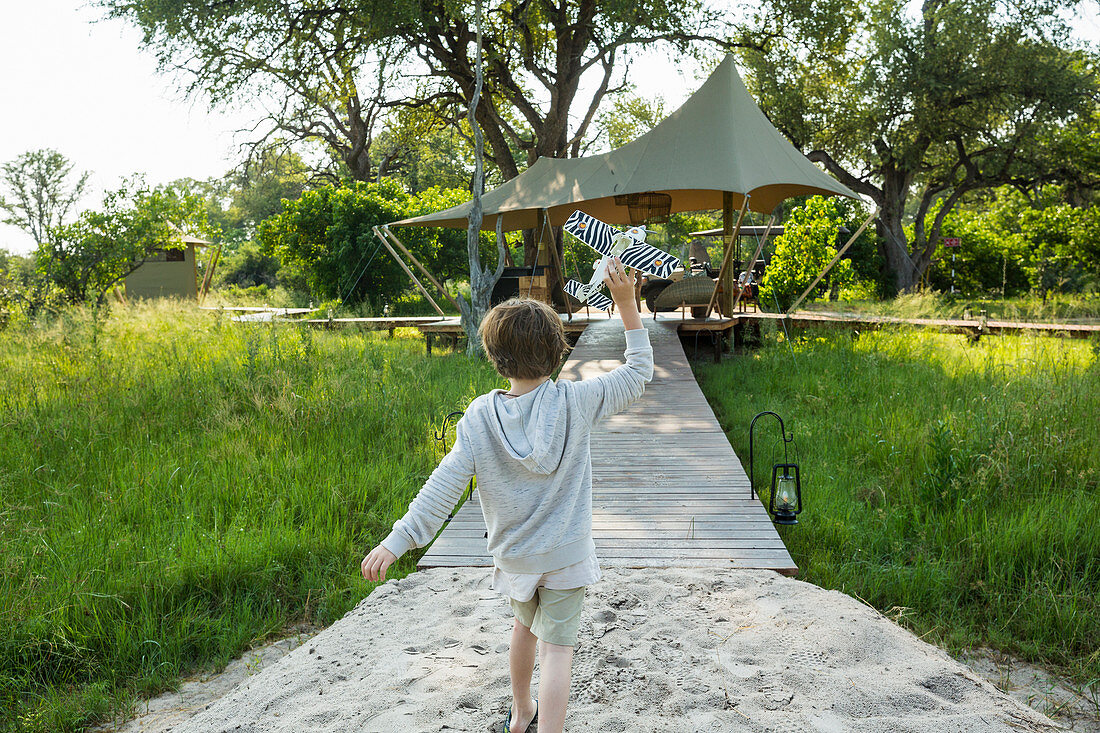 Sechsjähriger Junge spielt mit Spielzeugflugzeug, Zeltcamp, Botswana