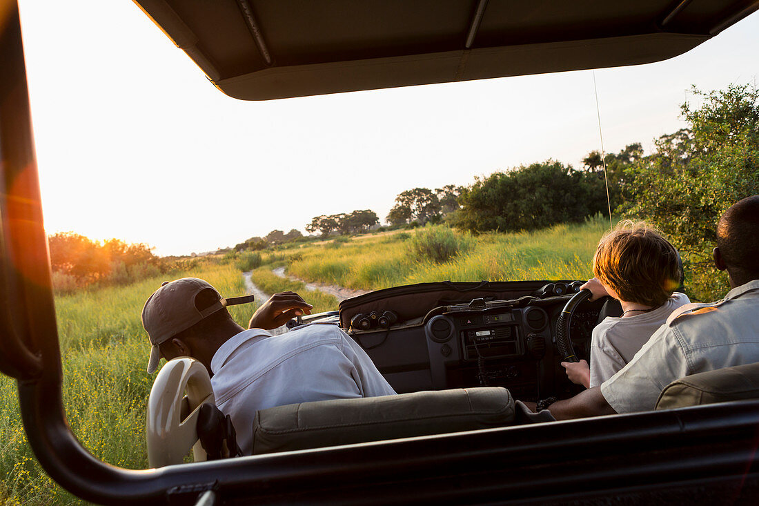 A six year old boy in the driving seat, steering safari vehicle at sunset, Botswana