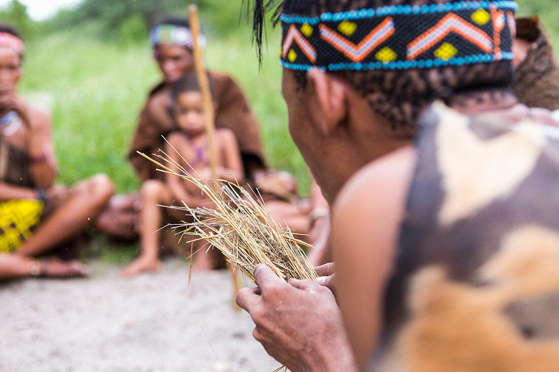 Ein Gruppe vom San-Volk, ein Mann beim traditionellen Feuermachen mit trockenem Gras
