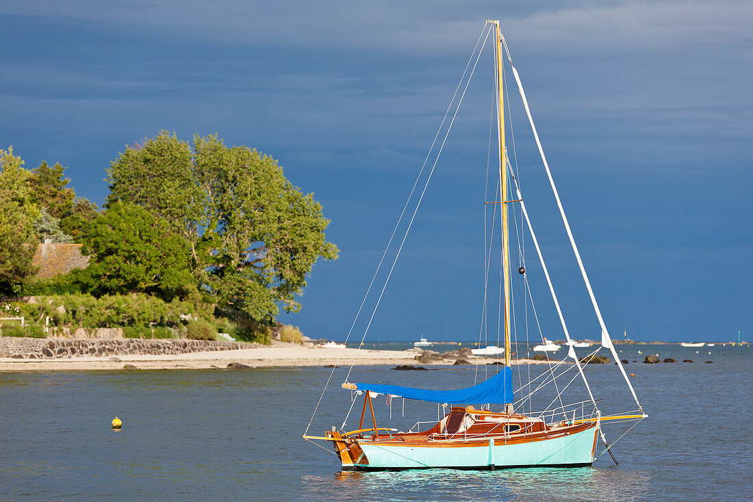 The sailing boat is anchored in a bay not far from the small port town of Saint Vaast la Hague.
