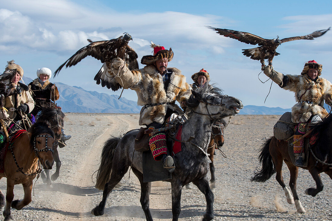 Eine Gruppe kasachischer Adlerjäger und ihre Steinadler zu Pferd auf dem Weg zum Steinadlerfest in der Nähe der Stadt Ulgii (Ölgii) in der Provinz Bajan-Ulgii in der westlichen Mongolei