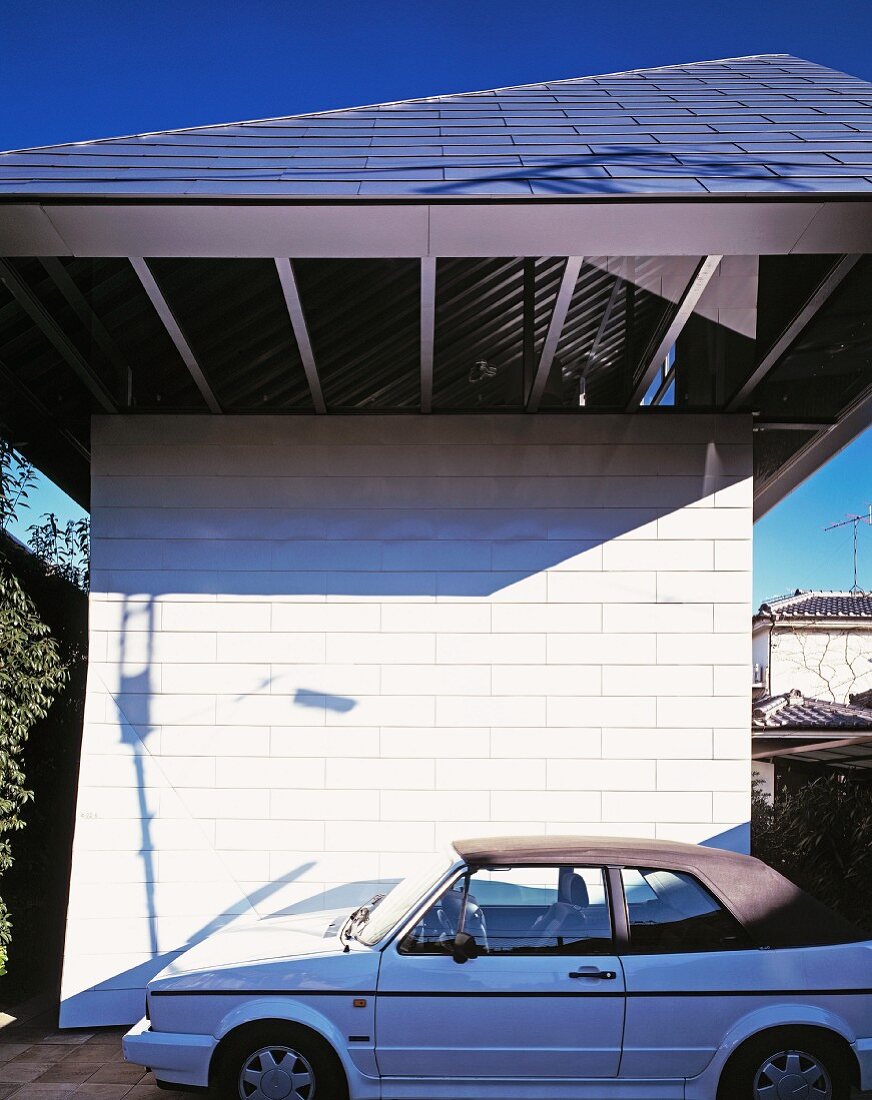 A parked car in front of a newly built house with a white facade and a green slate roof