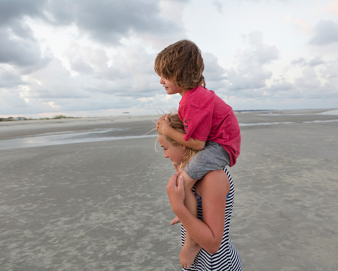 5 year old brother riding on his sister's shoulders at the beach, Georgia
