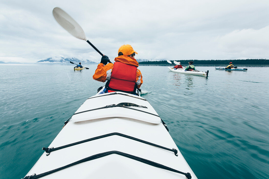 A person paddling in a double sea kayak on calm water off the coast of Alaska.