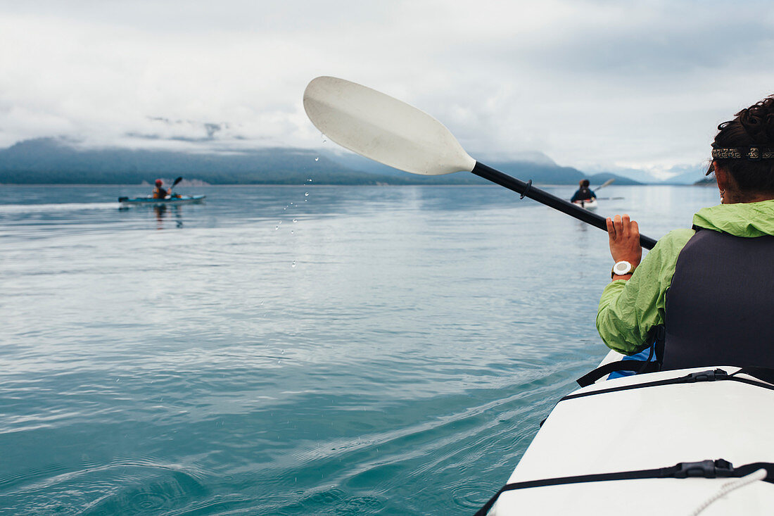 Group of sea kayakers paddling pristine waters of an inlet on the Alaska coastline.