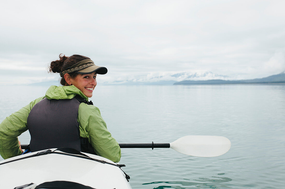 Happy female woman sea kayaking pristine waters of Muir Inlet in Glacier Bay National Park and Preserve, Alaska