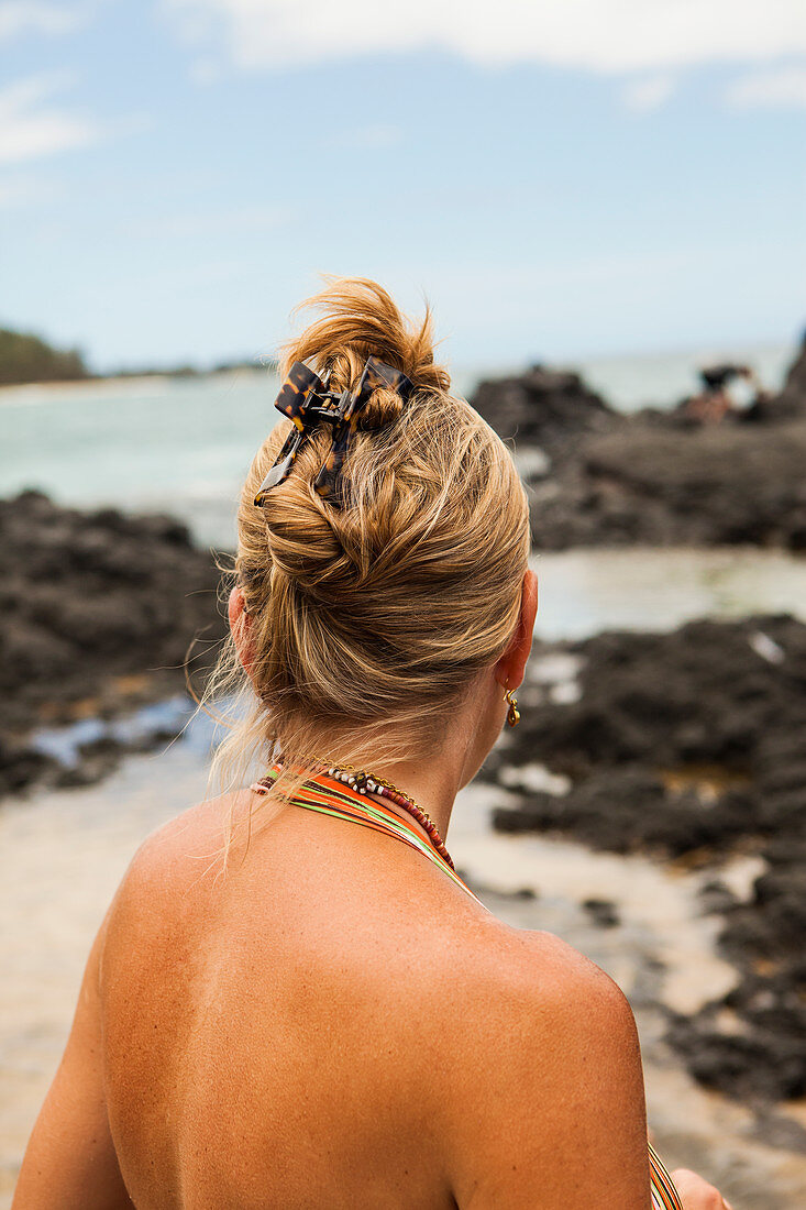 Rückansicht einer Frau an einem Strand mit Blick auf Felsen
