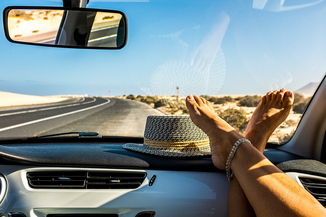 Weibliche Füße auf dem Armaturenbrett im fahrenden Auto