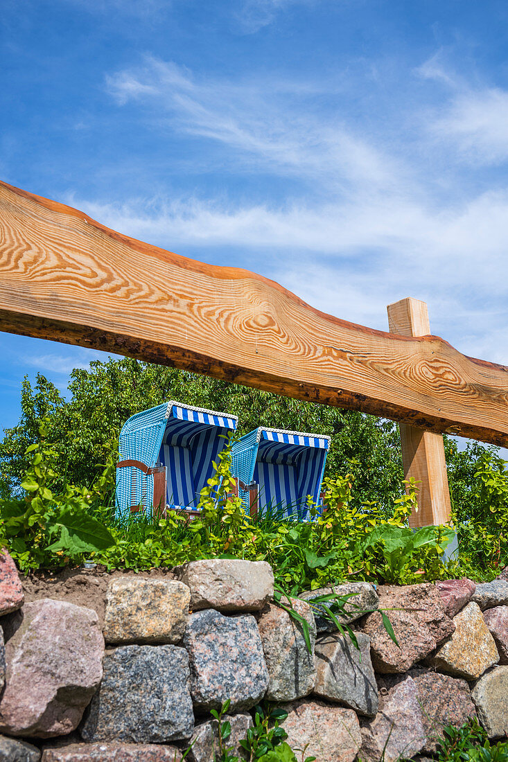 Two blue white beach chairs in the garden behind a wooden fence with a stone wall and blue summer sky, Usedom, Mecklenburg-Western Pomerania, Germany