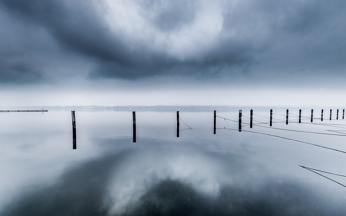 Reflecting UFO cloud over abandoned marina on a foggy winter morning at Lake Starnberg, Bavaria, Germany