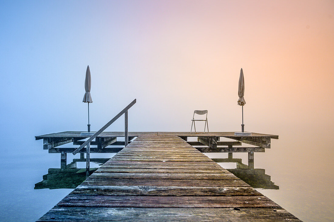 Steg mit eingeklappten Sonnenschirmen bei nebligen Sonnenaufgang am Starnberger See, Seeshaupt, Bayern, Deutschland