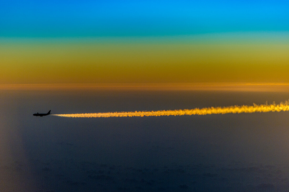 Flugzeug mit Kondensstreifen im Morgengrauen