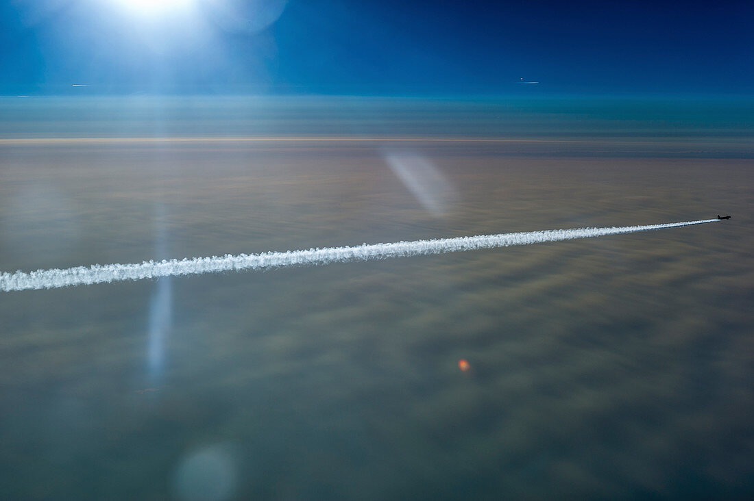 Airplane with contrails over closed cloud cover in the backlight