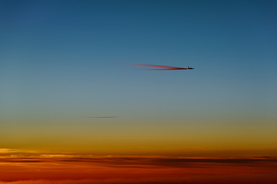 Flugzeug mit Kondensstreifen kurz vor dem Sonnenaufgang