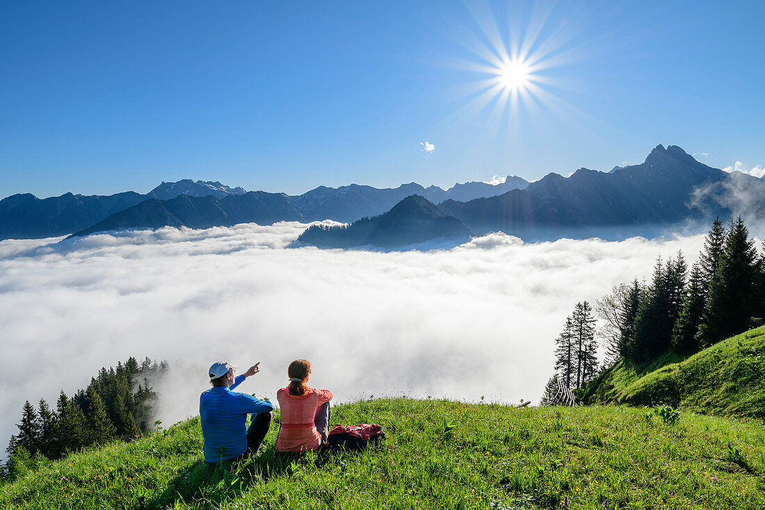 Mann und Frau sitzen auf Wiese und blicken auf Bergpanorama, Nebelmeer im Tal, Nebelhorn und Höfats im Hintergrund, am Himmelschrofen, Allgäuer Alpen, Allgäu, Bayern, Deutschland