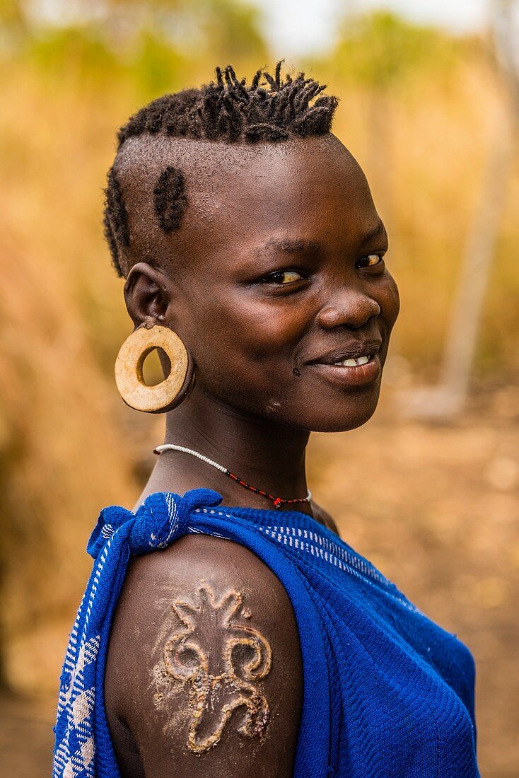 Mursi tribe woman with clay disc in her ear lobe and scarification on her shoulder, Lower Omo Valley, Mago National Park,  Ethiopia.