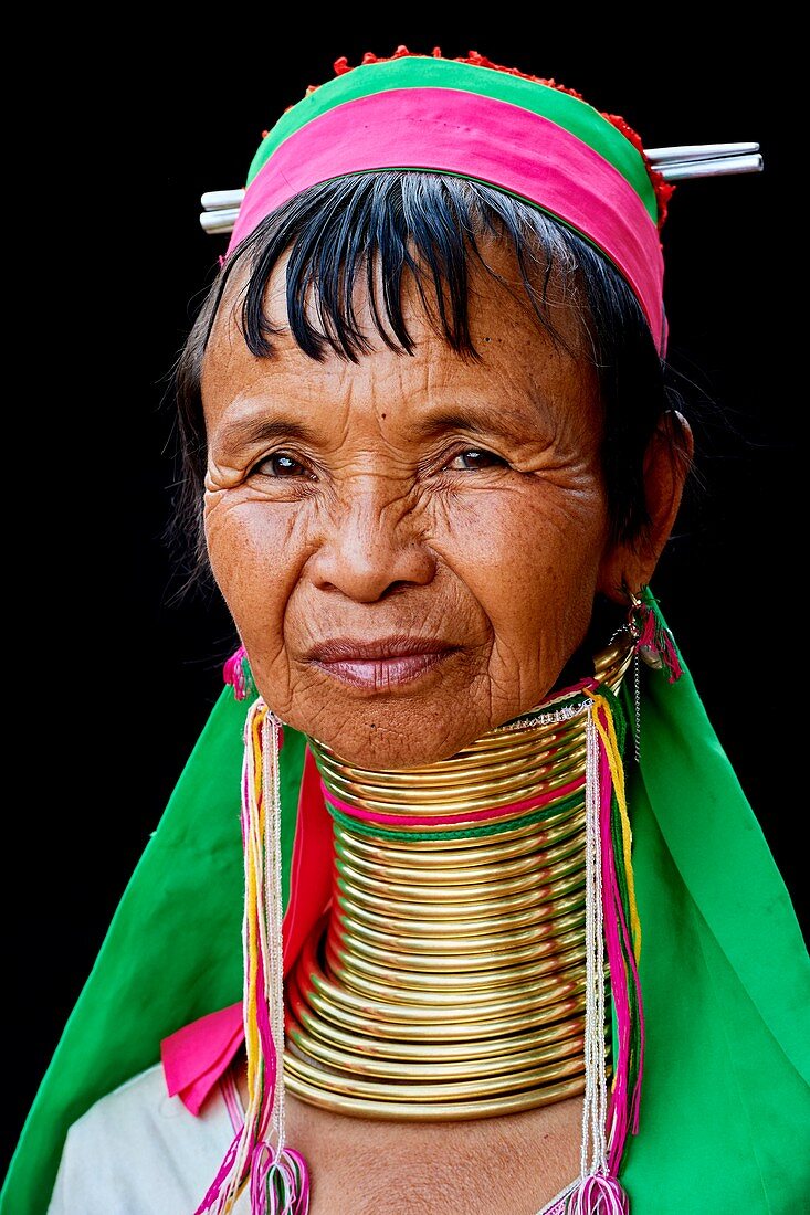 Porträt einer Frau aus Kayan Lahwi mit Messing-Halsschmuck und traditioneller Kleidung. Die Long Neck Kayan (auf burmesisch auch Padaung genannt) sind eine Untergruppe der Karen aus Burma. Sie tragen spiralförmige Windungen um den Hals und die Unterschenkel. Sie werden auch 'Giraffenfrauen' genannt. Der Hals selbst ist nicht verlängert; unter dem Druck des Kragens entsteht die Erscheinung eines gestreckten Halses, die Rippen senken sich und die Schultern und Schlüsselbeine kollabieren. Pan Pet Region, Bundesstaat Kayah, Myanmar