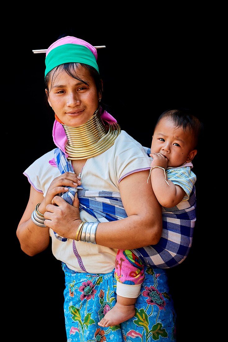 Kayan Lahwi woman carrying her baby and wearing brass neck coils and traditional clothing. The Long Neck Kayan (also called Padaung in Burmese) are a sub-group of the Karen ethnic from Burma. They wear spiral coils around their neck and lower legs.They are also nicknamed "giraffe women“. The neck itself is not lengthened; the appearance of a stretched neck is created under the pressure of the collar, the ribs lower and the shoulders and clavicles collapse.  Pan Pet Region, Kayah State, Myanmar