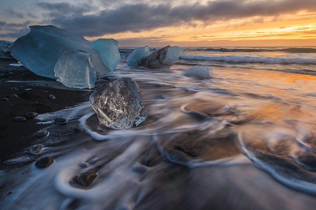 Gebrochenes Eis von angespülten Eisbergen am schwarzen Strand von Jokulsarlon bei Sonnenuntergang, Jokulsarlon, Südostisland, Island