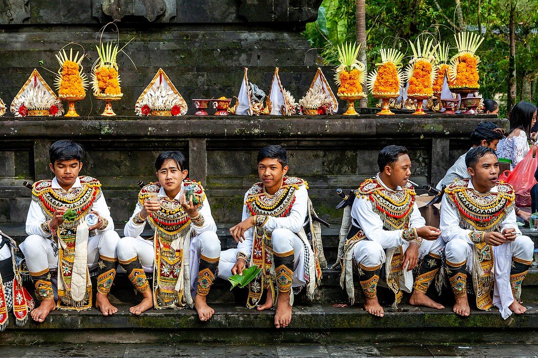 Eine Gruppe junger Männer in Kostümen beim Mittagessen auf einem Hindu-Festival, Wassertempel Tirta Empu, Bali, Indonesien