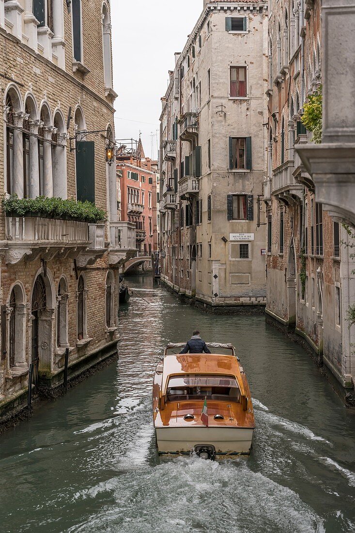cityscape with motorboat in narrow canal with historical buildings, shot in bright cloudy fall light at Venice, Veneto, Italy\n