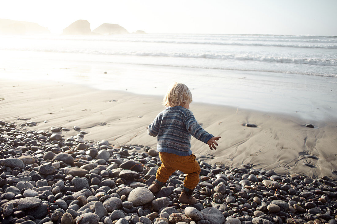 Little child plays on the autumnal beach in Big Sur, California, USA.