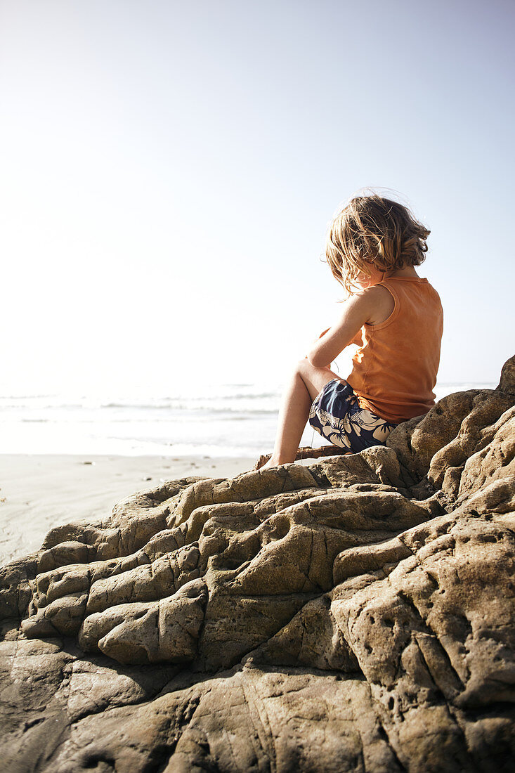 Kind sitzt auf einem Felsen am Strand von Big Sur, Kalifornien, USA.