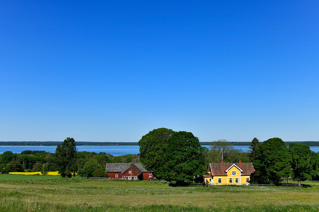 Blick auf einen Bauernhof mit Schwedenhaus und einen See bei Broddetorp, Schweden