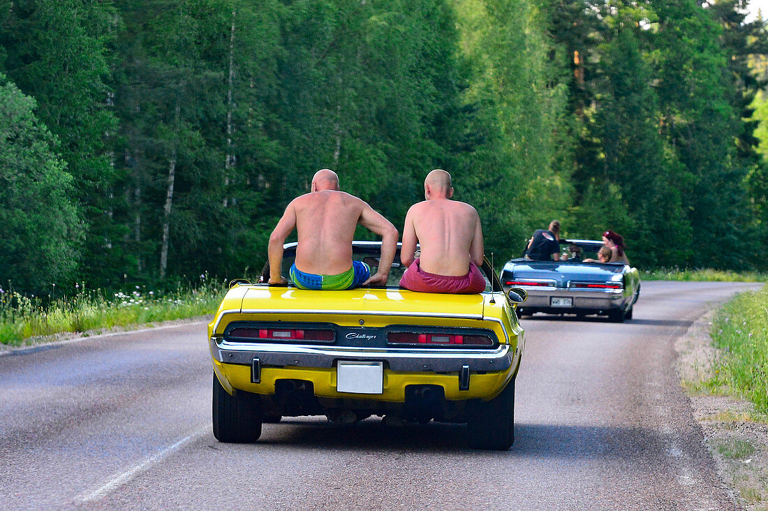 Two men sit on a vintage convertible while driving, Sollerön, Dalarna, Sweden