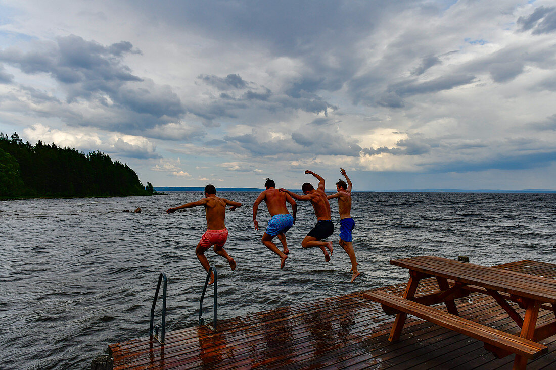 Vier Männer springen von einem Badesteg in den See, Siljansee, Sollerön, Dalarna, Schweden