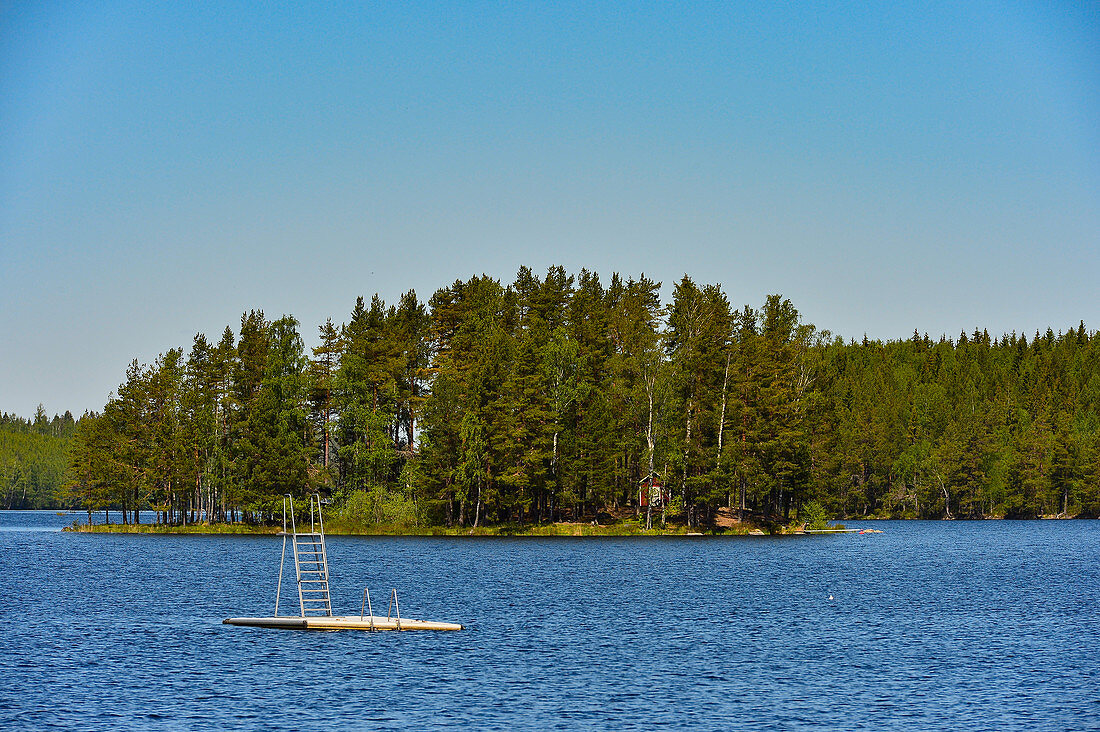 Eine kleine Badeplattform in einem See mit Insel umgeben von Wald, Provinz Örebro, Schweden