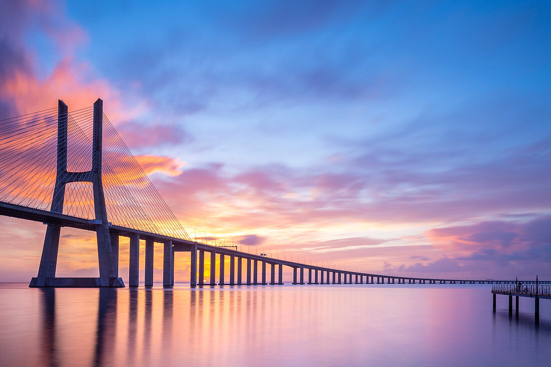 A colorful sunrise behind the Vasco da Gama bridge, reflected on the Tagus River. Lisbon, Portugal, Europe.