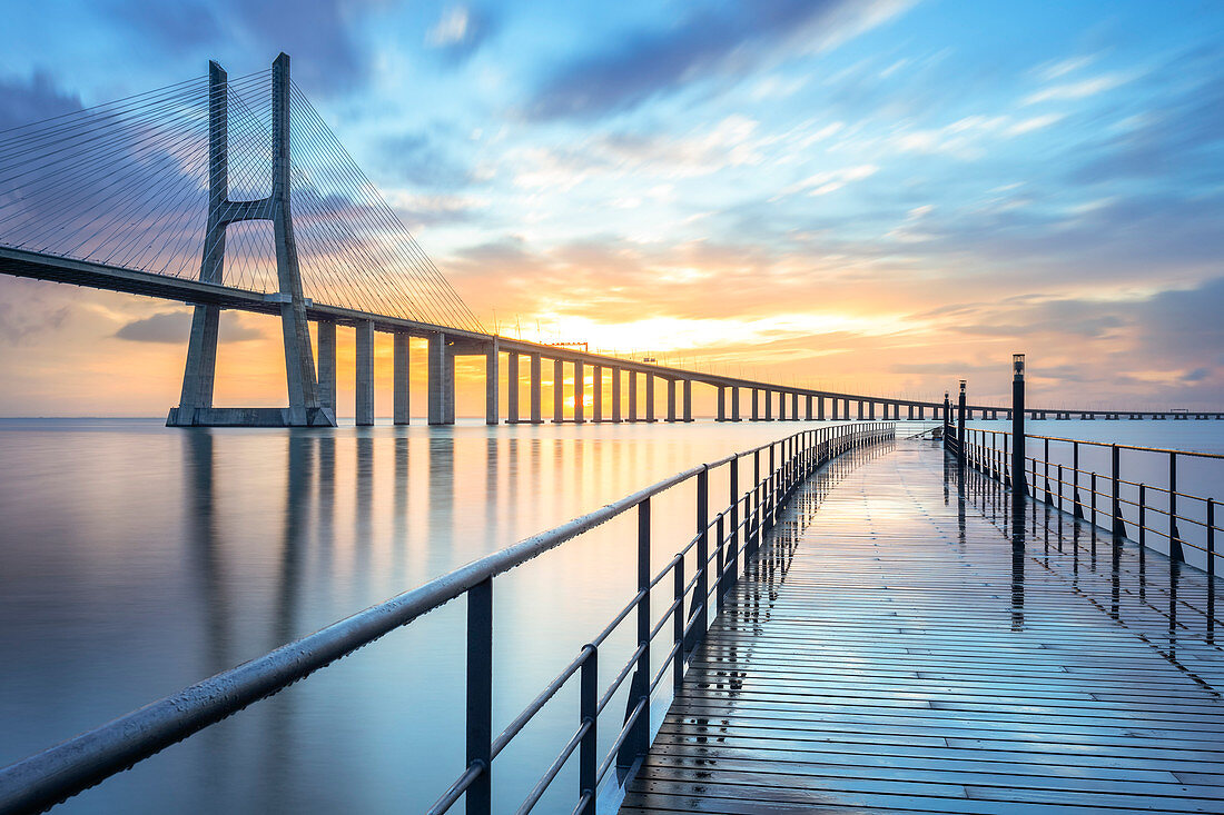 A colorful sunrise behind the Vasco da Gama bridge, reflected on the Tagus River. Lisbon, Portugal, Europe.