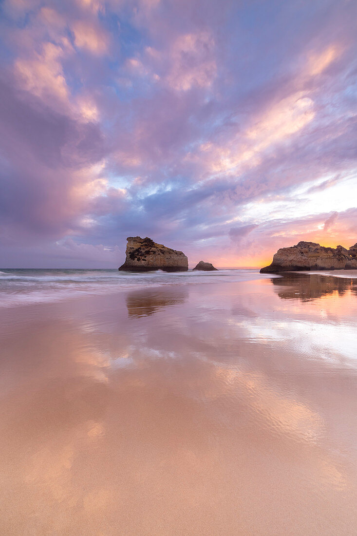 Ein bunter Sonnenuntergang spiegelt sich an den feuchten Ufern des Praia Dos Tres Irmaos wider, Alvor, Portimao, Algarve, Portugal, Europa
