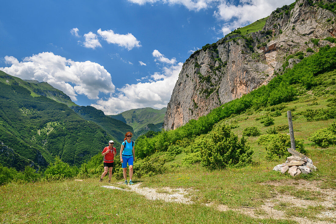 Man and woman hiking under rock face, Grande Anello dei Sibillini, Sibillini Mountains, Monti Sibillini, National Park Monti Sibillini, Parco nazionale dei Monti Sibillini, Apennines, Marche, Umbria, Italy