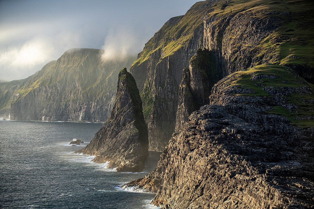 Steep coast in the west of the island of Vágar with the waterfall Bøsdalafossur and the rock needle Geitaskoradrangur near the largest lake in the Faroe Islands, Leitisvatn, Faroe Islands