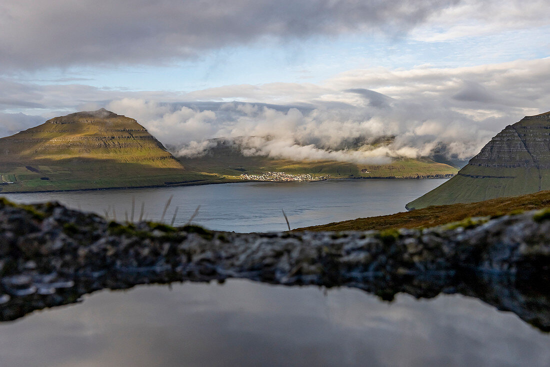 Blick vom Klakkur auf das Dorf Leirvík mit sonnendurchschienen Wolken und der typischen Graslandschaft, Färöer Inseln