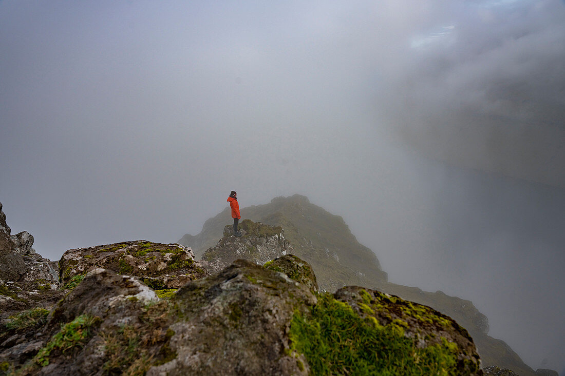 Wanderin steht an einem Felshang am Gipfel des Klakkur im Nebel, Klaksvík, Färöer Inseln