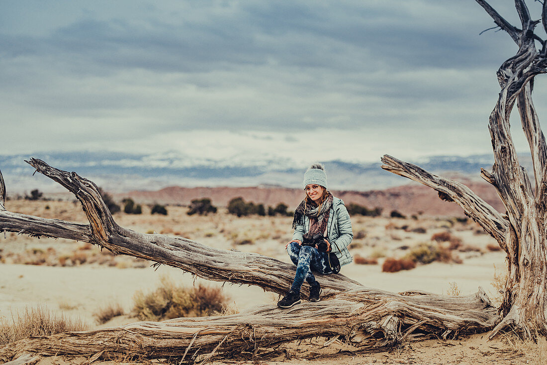 Woman sitting on parched trunk, desert landscape in Utah, USA, North America