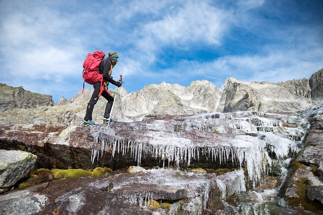 Wanderer überquert einen zugefrorenen Bach entlang des Sentiero Roma, Valle del Ferro, Val Masino, Valtellina, Provinz Sondrio, Lombardei, Italien