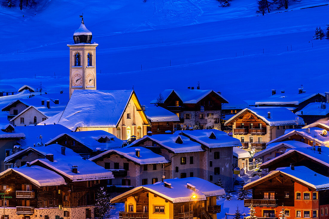Kirche und Häuser beleuchtet in der Dämmerung im Winter, Livigno, Valtellina, Lombardei, Italien, Europa