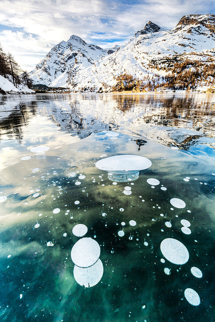 Methane bubbles in the icy surface of Silsersee with snowy peak. Lake Sils, Engadin Valley, canton of Graubunden, Switzerland, Europe.