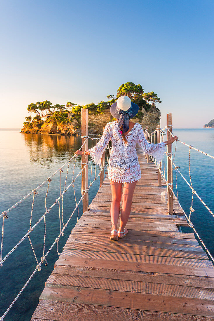 Junge Frau geht auf einer Hängebrücke aus Holz über dem Meer, die zur Insel Cameo führt, Agios Sostis, Zakynthos, Ionische Inseln, Griechenland, Europa