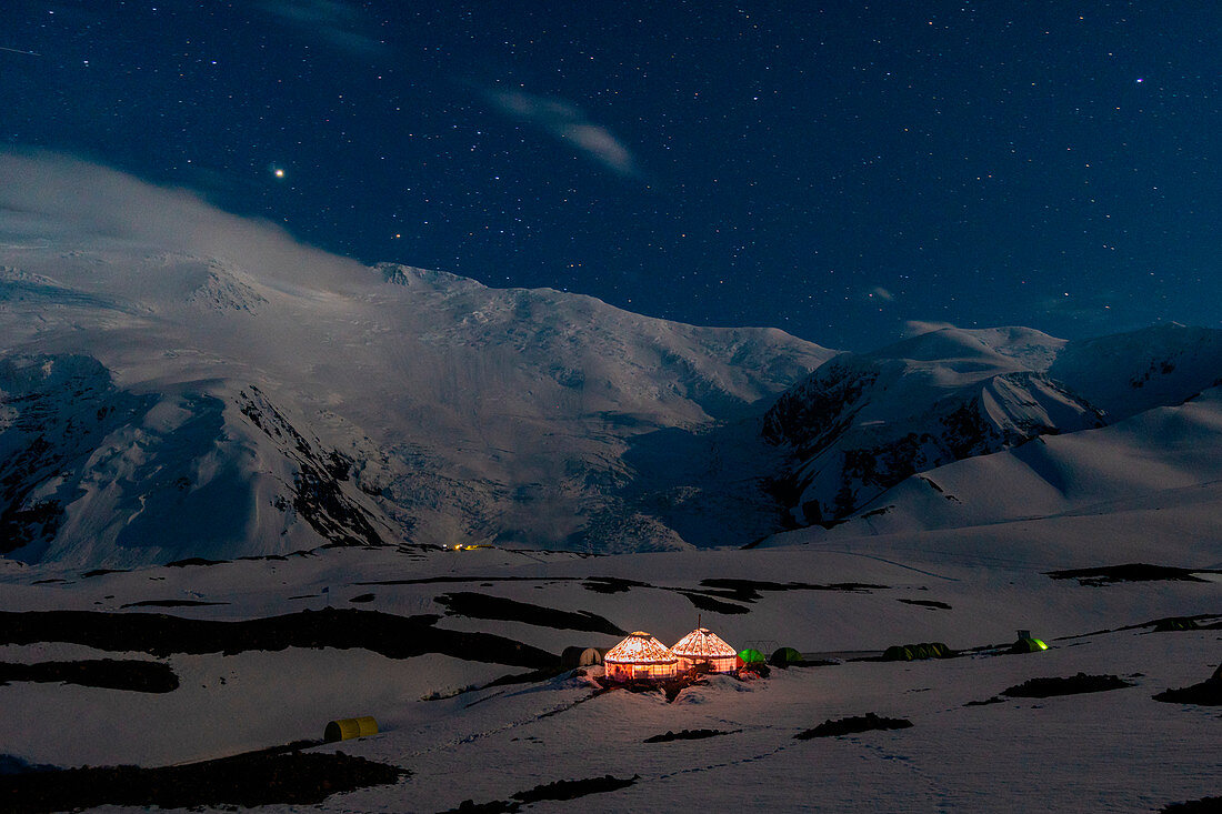 Nightscape of peak Lenin camp one with Peak Lenin massif in the background under a starring sky. Pamir, Kyrgyzstan, Central Asia. 