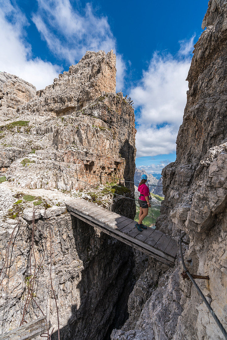 Junge Frau steht im Sommer auf einer Holzbrücke auf dem Klettersteig des Monte Paterno, Sextner Dolomiten, Trentino-Südtirol, Italien
